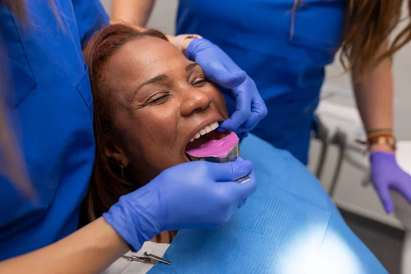 Close up of a female dentists hands, placing an impression tray into one of her black female clients mouth, in order to take a sample denture at the dental clinic