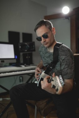 Müzik yapımcısı kendi stüdyosunda yeni bir proje kaydederken elektro gitarla akor tıngırdatıyor.