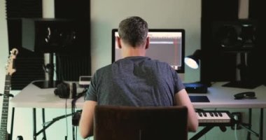 Music producer seen from behind while working on a project with the computer at his home studio