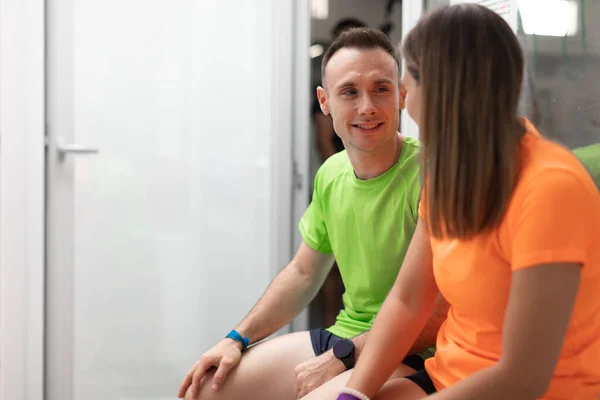 A couple of gym trainees talking during a break sitting on a bench at the crossfit box