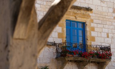 Balkonda kırmızı çiçekli mavi pencereli eski evin güzel manzarası, Dordogne 'daki Monpazier köyü.