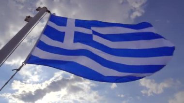 The blue and white Greek flag flutters in the wind during a cruise to the Cyclades, in background the blue sky and clouds