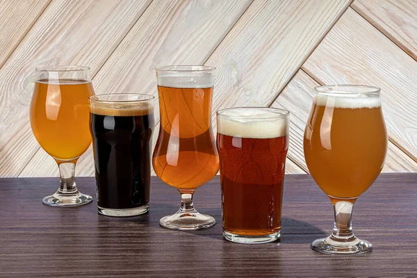 Ochelari cu diferite tipuri de bere artizanală pe un bar de lemn. În pahare şi sticle. Nuci şi biscuiţi pe masă. Pe un fundal întunecat. Fotografie de stoc