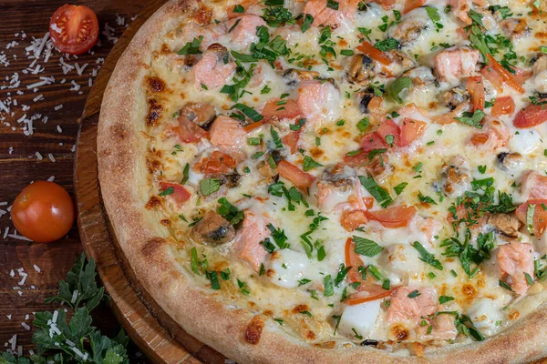 Пицца кальцоне с беконом и сыром, травами и помидорами черри. С моцареллой, креветками и осьминогами, мидиями и другими продуктами на деревянном фоне. — стоковое фото