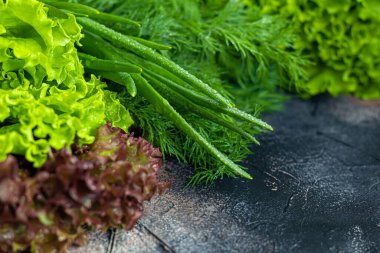 Fresh vegetables for salad. Tomatoes and lettuce, cucumbers with zucchini and cabbage with dill. Spring harvest, benefits and vitamins. On a dark background.