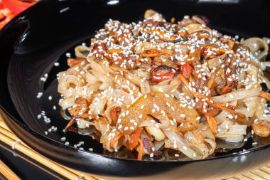 Udon noodles with meat, mushrooms and vegetables. Sprinkled with sesame seeds. Asian food, roast on black background, copy space