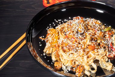 Udon noodles with meat, mushrooms and vegetables. Sprinkled with sesame seeds. Asian food, roast on black background, copy space