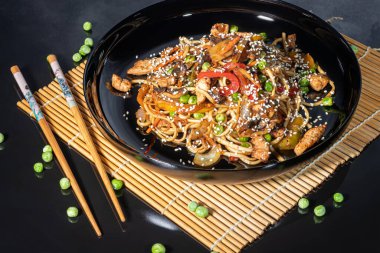 Udon noodles with meat, mushrooms and vegetables. Sprinkled with sesame seeds. Asian food, roast on black background, copy space