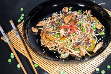 Udon noodles with meat, mushrooms and vegetables. Sprinkled with sesame seeds. Asian food, roast on black background, copy space