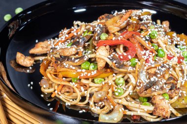 Udon noodles with meat, mushrooms and vegetables. Sprinkled with sesame seeds. Asian food, roast on black background, copy space