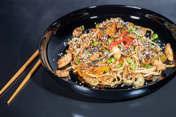 Udon noodles with meat, mushrooms and vegetables. Sprinkled with sesame seeds. Asian food, roast on black background, copy space