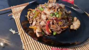 Udon noodles with meat, mushrooms and vegetables. Sprinkled with sesame seeds. Asian food, roast on black background, copy space
