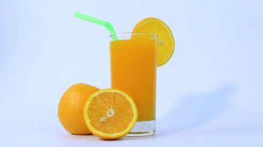 Bir bardak portakal suyu, portakal dilimlenmiş, beyaz arka planda, yeşil boru görüntüleriyle.