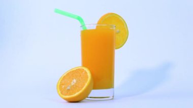Bir bardak portakal suyu, portakal dilimli meyve, beyaz arka planda izole edilmiş yeşil boru görüntüleriyle.