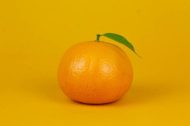 An Orange fruit with green leaf isolated on yellow background. One orange fruit with leaf stand on isolating concept for ads design