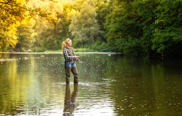 Una mujer se para en el río y pesca con una varilla giratoria — Foto de Stock