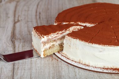 Tiramisu keki, dilimlenmiş bir pasta ve gri arka planda bir bıçak, yakın plan.