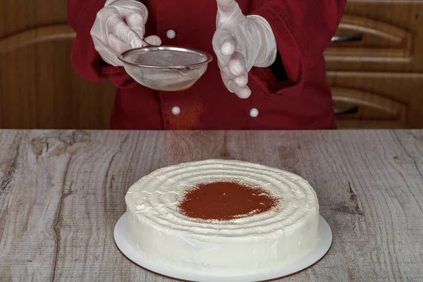 Confectioner decorates white cream cake cocoa powder — Stock Photo, Image