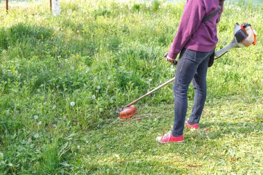 Kadın çiftçi arka bahçedeki çimleri tel biçme makinesiyle biçiyor.