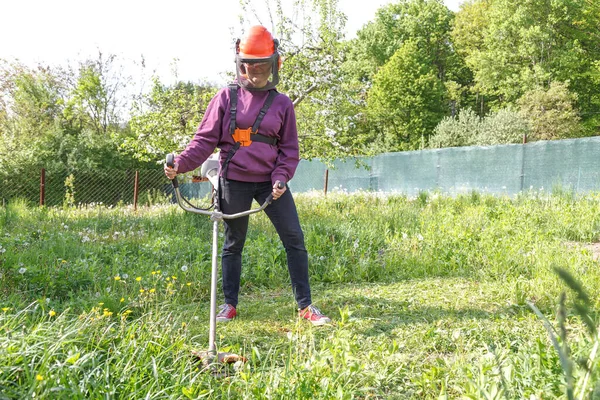 Woman farmer mows the grass in the backyard using string trimmer — Stockfoto