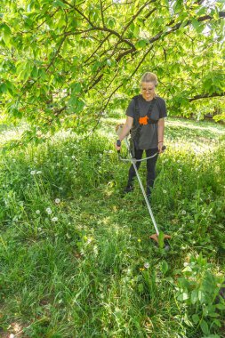 Bir kadın arazisinde benzin makası ile çim biçiyor.