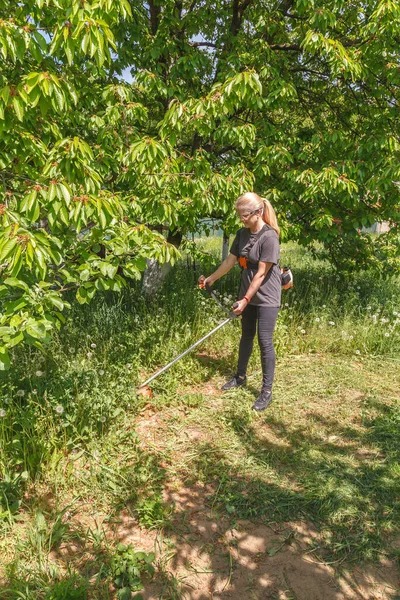 A woman mows grass on his property with a gasoline trimmer — Stok Foto