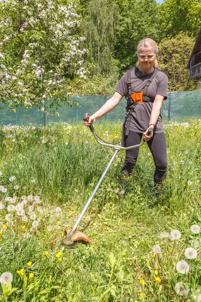 A woman mows grass on his property with a gasoline trimmer — Stok Foto