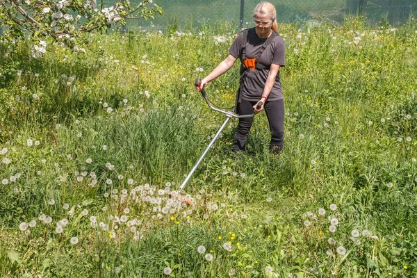 Seorang wanita memotong rumput di tanah miliknya dengan pemangkas bensin — Stok Foto
