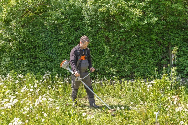 A man mows grass on his property with a gasoline trimmer — Stockfoto