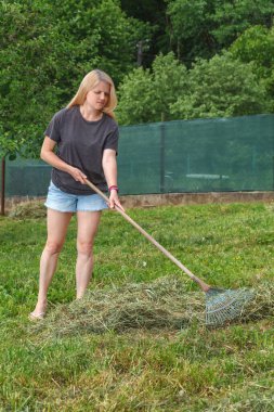 Ilık bir bahar gününde bahçede taze kesilmiş çimenleri seçen bir kız. Bahçe işleri..