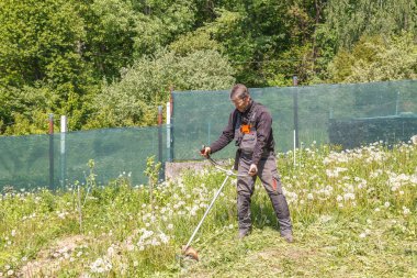 Bir adam bahçedeki çimleri benzin makası ile biçiyor. Gözlerini korumak için gözlük takıyordu. Baharda bahçede çalış..