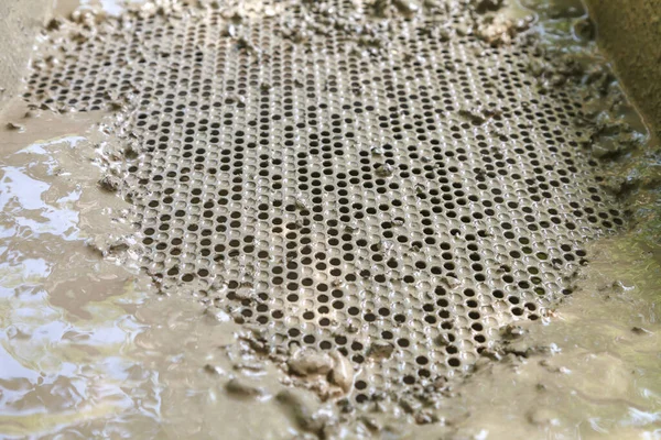 Metal sieve with round holes to clean dirty water from small stones. Cleaning process of stones and clay