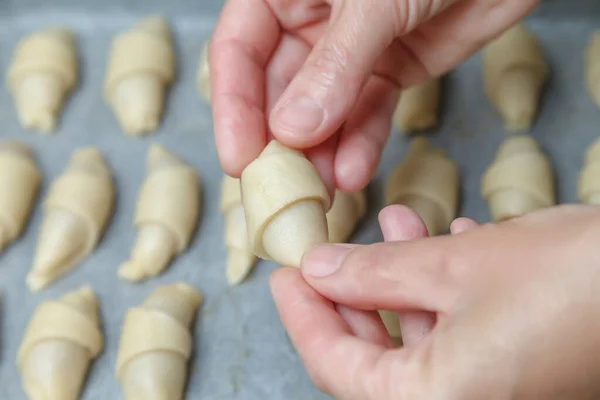 The hands of the pastry chef roll the dough with filling into a roll for further baking croissants. French mini croissants with fruity jam. Close up. Homemade baking concept