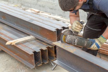 Elleri sıcak kıvılcımlardan korumak için koruyucu gözlüklü ve eldivenli bir adam inşaat alanında metal kesiyor.