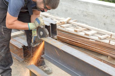 Elleri sıcak kıvılcımlardan korumak için koruyucu gözlüklü ve eldivenli bir adam inşaat alanında metal kesiyor.