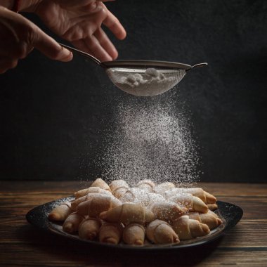 Kadınların elleri yeni pişmiş Fransız kruvasanlarının üzerine elek ile şeker serpiyor. Ev yapımı pişirme konsepti