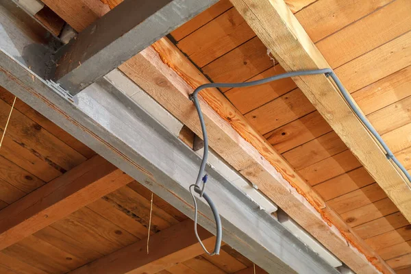 Construction of a residential building. The metal beam supports the wooden ceiling of the second floor. The electrical cable in the protective sleeve is attached to the ceiling.