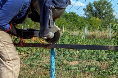 Ağır bir endüstri işçisi, şantiyesinde elektrikli değirmen ile kaynak yapıyor. Maske ve koruyucu eldivenler göz ve ellerdeki kıvılcımlara karşı korur.
