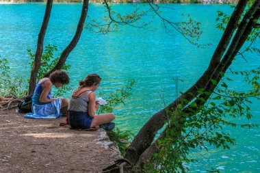 PLITVICE, CROATIA - 13 Eylül 2016: Tanımlanamayan genç kadınlar Plitvice Gölleri Ulusal Doğa Koruma Alanındaki göllerden birinin kıyılarında dinleniyor.