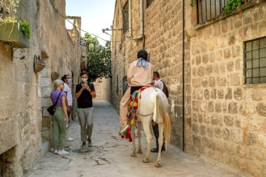 MARDIN, TURKEY - 10 Ekim 2020: Tanımlanamayan turistler eski kasabadaki dar bir sokakta ata biniyorlar.
