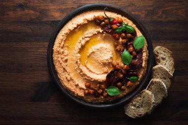 Dried tomato hummus garnished with caramelized chickpeas on a plate. Brown wooden background