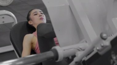 Young attractive athletic asian woman training her leg quads using leg press machine at the gym. Slow motion. Healthcare, fitness and bodybuilding concept.