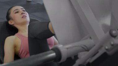 Young attractive athletic asian woman training her leg quads using leg press machine at the gym. Slow motion. Healthcare, fitness and bodybuilding concept.