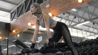 Young attractive athletic asian woman training her arms and upper body using dumbbells at the gym. Slow motion. Healthcare, fitness and bodybuilding concept.