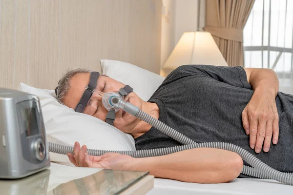 Middle age male with sleep apnea wearing CPAP headgear and mask while sleeping in his bedroom