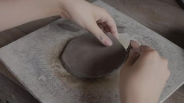 Close up of female teenager's hands working on making clay pottery using simple pottery tools