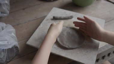 Close up of female teenager's hands working on making clay pottery using simple pottery tools