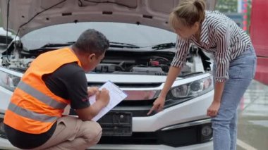 Worried young Asian woman talking to a car insurance agent or technician to claim the repair on her car accident