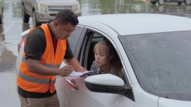 Male car insurance agent asking the female car owner to sign the car insurance claim form while she is sitting in the car on a raining day