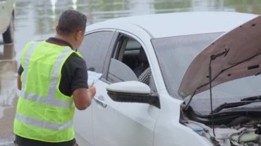 Male car insurance agent asking the female car owner to sign the car insurance claim form while she is sitting in the car on a raining day
